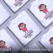 Футболка найсолодша вередуля, білого кольору, зображена з фронтального ракурсу на манекені, фон має легкий градієнт, принт з малюнком дівчинки у рожевій сукні з серйозним виразом обличчя та написом 'НАЙСОЛОДША ВЕРЕДУЛЯ У СВІТІ'.