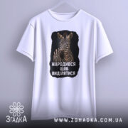 Футболка народився щоб виділятися, біла футболка з принтом зебри на чорному фоні, з ракурсу спереду, підвішена на вішалці, на світлому фоні.