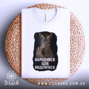 Футболка народився щоб виділятися, складена біла футболка з принтом зебри, з ракурсу зверху, на плетеній основі, з етикеткою видимою на горловині.