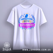 Футболка народжена бути королевою, білого кольору, підвішена на вішалці, фон світло-сірий, принт з короною та написом в яскравих кольорах: синьому, рожевому та золотому.