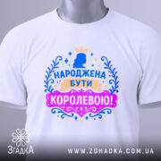 Футболка народжена бути королевою, білого кольору, складена на плоскій поверхні, фон світлий, принт з короною та написом в яскравих кольорах: синьому, рожевому та золотому, з видимою етикеткою.