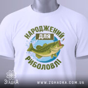 Футболка народжений для риболовлі, білого кольору, зображена зверху, на ній видно етикетку, фон світло-сірий, принт з рибою та текстом в зелених відтінках.