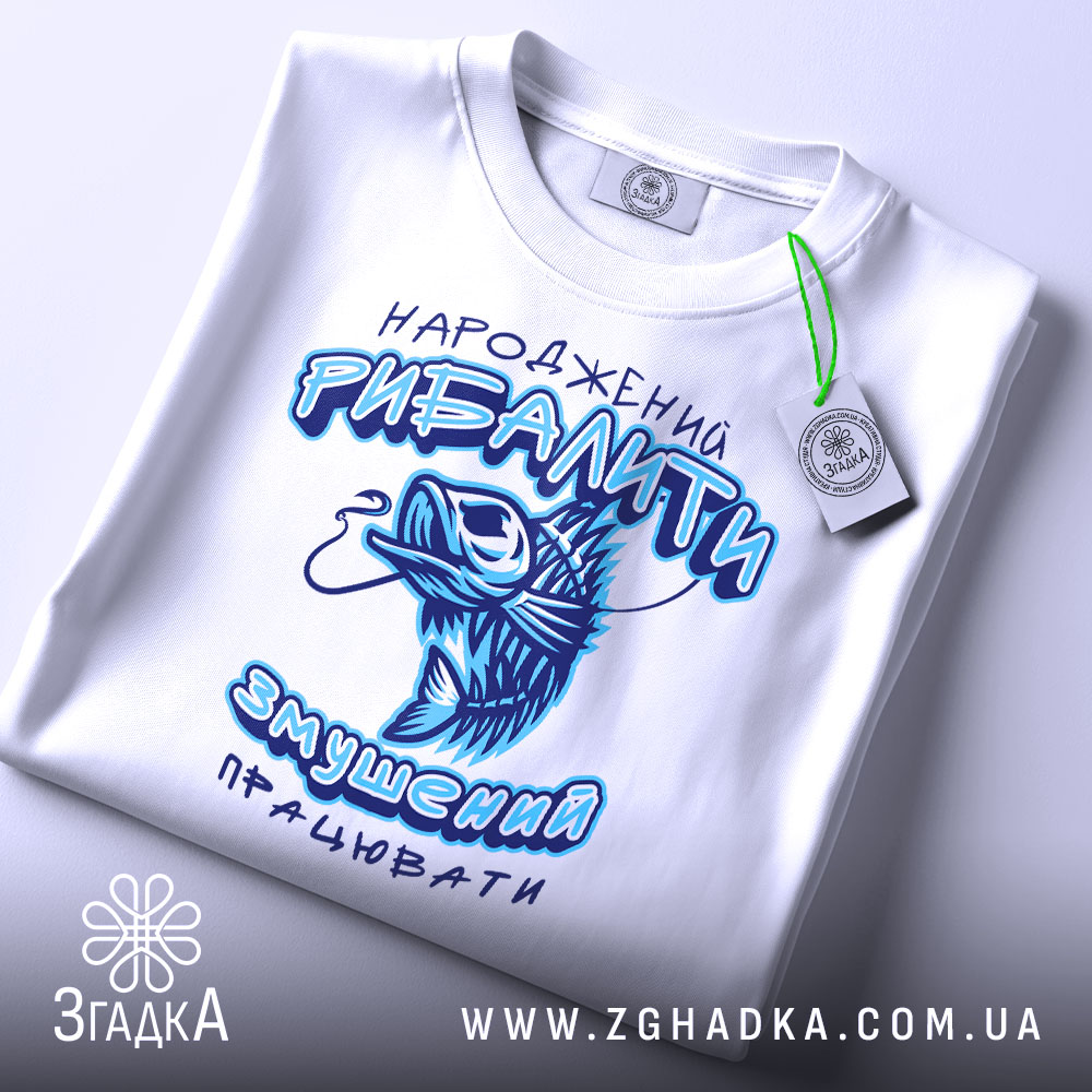 Футболка народжений рибалити, білого кольору, складена на поверхні, фон світлий, принт з рибою та текстом у блакитних відтінках, на футболці є етикетка з зеленим шнурком.