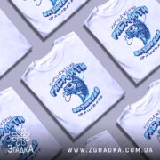 Футболка народжений рибалити, білого кольору, зображена з близького ракурсу на манекені, фон нейтральний, принт з рибою та текстом виконаний у блакитних тонах.