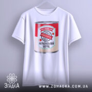 Футболка наш борщ. Біла футболка, підвішена на вішалці, з принтом банки борщу. Принт яскравий, з червоним та зеленим кольорами, на фоні світло-сірого кольору.