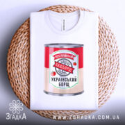 Футболка наш борщ. Біла футболка, складена на плетеній кошику, з принтом банки борщу. Принт яскравий, з червоними помідорами та написом '100% український'.