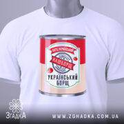 Футболка наш борщ. Біла футболка, складена на поверхні, з принтом банки борщу. Принт яскравий, з червоними помідорами та написом '100% український'. На футболці є етикетка з зеленим шнурком.