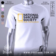 Футболка National Sarcasm Society білого кольору, зображена на манекені з блискучою поверхнею, фон світло-сірий, принт містить чорний текст з жовтим логотипом National Geographic та жовтим написом 'LIKE WE NEED YOUR SUPPORT'.