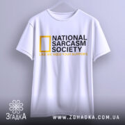 Футболка National Sarcasm Society білого кольору, підвішена на вішалці, фон світло-сірий, принт містить чорний текст з жовтим логотипом National Geographic та жовтим написом 'LIKE WE NEED YOUR SUPPORT'.