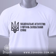 Футболка національне агентство, біла, зображена на манекені, фон нейтральний, принт чорного кольору з текстом та тризубом.