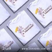 Футболка не бахнута унікальна, білого кольору, зображена з фронтального ракурсу на манекені, фон світло-сірий, принт з дівчинкою у кімоно, яка виконує удар, текст чорного кольору: 'НЕ БАХНУТА, А УНІКАЛЬНА!'