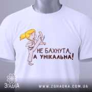 Футболка не бахнута унікальна, білого кольору, складена на поверхні, фон світло-сірий, принт з дівчинкою у кімоно, яка виконує удар, текст чорного кольору: 'НЕ БАХНУТА, А УНІКАЛЬНА!', на комірці видно етикетку.