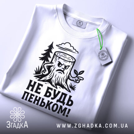 Футболка не будь пеньком. Біла футболка з чорним принтом, зображення пенька з гілочкою та написом розташоване на грудях. Вид зверху, на футболці є етикетка з зеленим шнурком. Фон світлий.