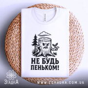 Футболка не будь пеньком. Біла футболка з чорним принтом, зображення пенька розташоване на плоскій поверхні з плетеного матеріалу. Фон світлий, що підкреслює текстуру футболки та принта.