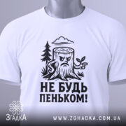 Футболка не будь пеньком. Біла футболка з чорним принтом, зображення пенька з гілочкою та написом розташоване на грудях. Вид зверху, на футболці є етикетка з зеленим шнурком. Фон світлий.