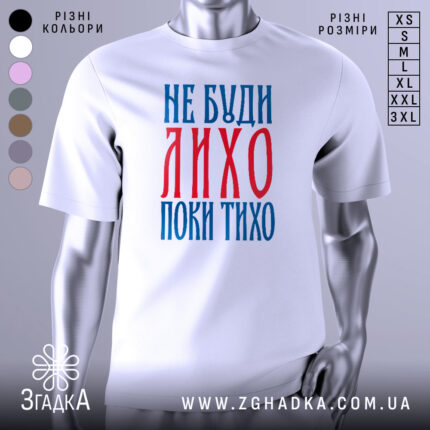 Футболка не буди лихо білого кольору, зображена з фронтального ракурсу на манекені, фон світло-сірий, принт червоного та синього кольорів з текстом 'НЕ БУДИ ЛИХО ПОКИ ТИХО'.