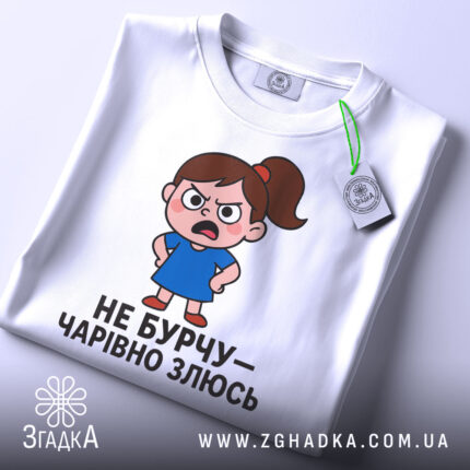 Футболка не бурчу. Біла футболка, зображена з верхнього ракурсу, на ній малюнок сердитої дівчинки в синій сукні, текст чорного кольору, на комірці видно етикетку.