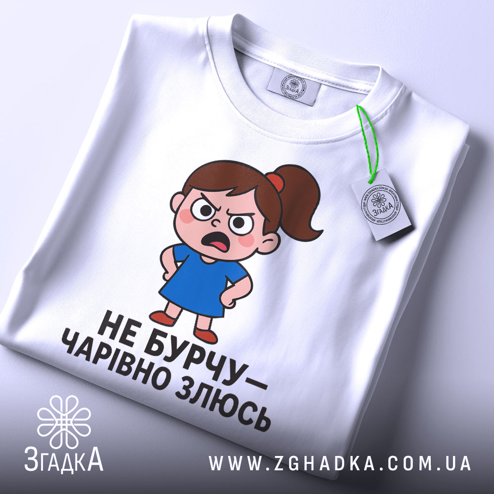 Футболка не бурчу. Біла футболка, зображена з верхнього ракурсу, на ній малюнок сердитої дівчинки в синій сукні, текст чорного кольору, на комірці видно етикетку.