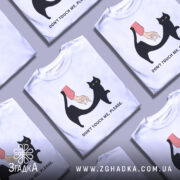 Футболка не чіпай. Біла футболка на манекені, з принтом чорного кота та руки, що його торкається. Фон світло-сірий, принт яскравий, текст під ним чорний.