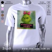 Футболка не чіпайте бантик. Біла футболка з принтом, на якому зображений зелений персонаж з рожевим бантиком на голові. Фон розмитий, з відтінками зеленого та блакитного. Текст на принті чорного кольору з білим шрифтом.