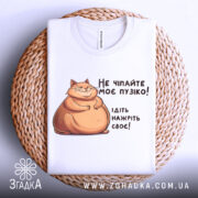 Футболка не чіпайте пузіко. Біла футболка, складена на плетеній основі, з принтом кота та текстом. Фон світлий, створює затишну атмосферу.