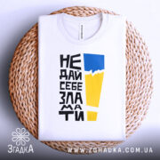 Футболка не дай себе зламати. Біла футболка, складена на плоскій поверхні, зображена зверху. На фоні світло-сірого кольору з плетеним кошиком. Принт з чорного тексту, жовтого і блакитного кольорів, розташований по центру.