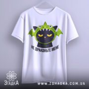 Футболка не драконьте мене, біла, підвішена на вішалці, фон світлий, принт з чорним котом у зеленій драконячій шапці, з виразом незадоволення.