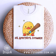 Футболка не дратуйте пташку, біла, складена на плетеній кошику, фон світло-сірий, принт з жовтим каченям, яке тримає биту, текст червоним шрифтом.
