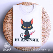 Футболка не дратуйте, білого кольору, складена на плетеній кошику, фон світло-сірий, принт з чорним котом з червоним ножем, текст під котом чорного кольору, видно етикетку з написом.