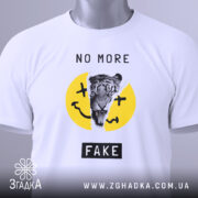 Футболка не фейк. Біла футболка, складена на столі, з принтом тигра на жовтому фоні, текстом 'NO MORE FAKE' над принтом і чорним написом 'FAKE' внизу. На футболці є етикетка з зеленим шнурком. Фон світло-сірий.