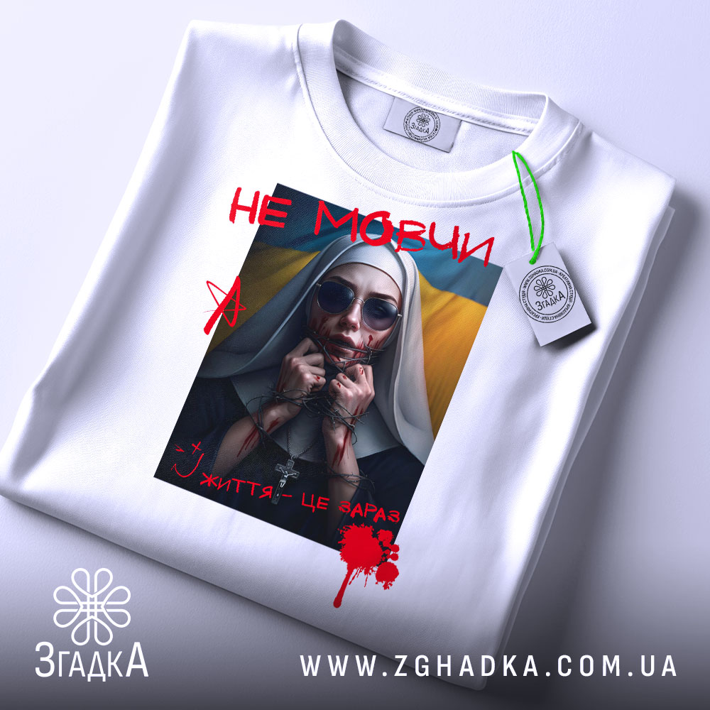Футболка не мовчи подарунок, біла, складена на поверхні, фон світло-сірий, принт з зображенням жінки в чорному одязі з червоними плямами, написом 'НЕ МОВЧИ' і українським прапором на фоні, з етикеткою.