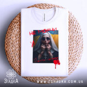 Футболка не мовчи подарунок, біла, складена на плетеному кошику, фон білий, принт з зображенням жінки в чорному одязі з червоними плямами, написом 'НЕ МОВЧИ' і українським прапором на фоні.