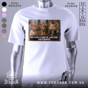 Футболка не нам судити. Біла футболка з коротким рукавом, зображення на грудях показує трьох персонажів з анімаційного фільму, які сидять за столом. На фоні видно вікно з жалюзі.