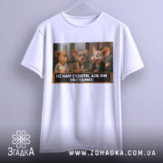 Футболка не нам судити. Біла футболка, підвішена на вішалці, з принтом трьох персонажів, які сидять за столом. На фоні видно вікно з жалюзі.