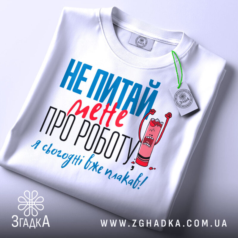 Футболка не питай мене, біла, з коротким рукавом, на столі, фон світло-сірий, принт з текстом червоного та блакитного кольорів, з малюнком олівця, що кричить, з етикеткою на шнурку.