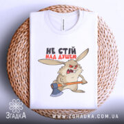 Футболка не стій над душею, біла, складена на плетеній кошику, фон світло-сірий, принт з кроликом з сокирою, текст чорного та червоного кольору.