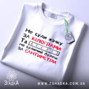 Футболка не суди жінку, біла, зображена зверху, фон світлий, принт чорного та червоного кольорів з текстом і етикеткою.