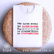 Футболка не суди жінку, біла, зображена на плетеній основі, фон нейтральний, принт чорного та червоного кольорів з текстом.