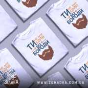 Футболка не ти без бороди. Біла футболка з коротким рукавом, зображена на манекені з нейтральним фоном. Принт містить текст 'ТИ не ти КОЛИ БЕЗ БОРОДИ' з малюнком бороди, виконаним у коричневих тонах.