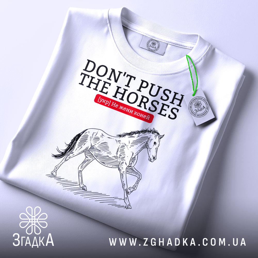 Футболка не жени коней, біла, зображена на столі, фон світлий, принт з конем у стилі малюнка, текст червоний на чорному.