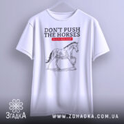 Футболка не жени коней, біла, підвішена на вішалці, фон однотонний, принт з конем у стилі малюнка, текст червоний на чорному.