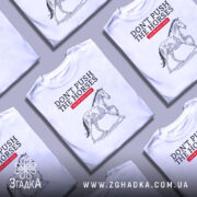 Футболка не жени коней, біла, зображена на столі, фон світло-сірий, кілька футболок в одному кадрі, принт з конем у стилі малюнка, текст червоний на чорному.