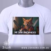Футболка не зли лисичку. Біла футболка, складена на поверхні, принт з лисичкою з бензопилами, зелений тег на комірці, фон світлий.