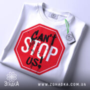 Футболка не зупинити, біла, складена на поверхні, з видимим етикеткою, фон світло-сірий, принт червоного кольору у формі знака стоп з написом 'CAN'T STOP US!' чорними буквами та плямами фарби.