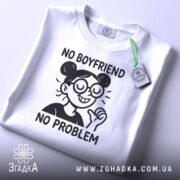 Футболка немає хлопця немає проблем, складена біла футболка, фон світло-сірий, принт з дівчиною в окулярах, текст чорного кольору, на футболці є етикетка з зеленим шнурком.