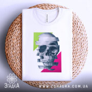 Футболка неоновий череп, біла, складена на плетеній кошику, фон світло-сірий, принт з черепом, розділеним на смуги, з яскравими зеленими та рожевими геометричними формами.