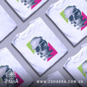 Футболка неоновий череп, біла, зображена на манекені з бокового ракурсу, фон світло-сірий, принт з черепом, розділеним на смуги, з яскравими зеленими та рожевими геометричними формами.