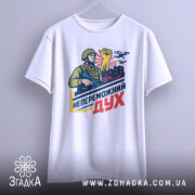 Футболка непереможний дух, білого кольору, підвішена на вішалці, фон світло-сірий, принт з військовим, що тримає автомат і піднятою рукою, на фоні червоні будівлі та дрони.