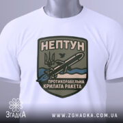 Футболка нептун крилата ракета, біла, зображена зверху, на ній прикріплений тег, фон світло-сірий, принт з зображенням ракети та текстом на темно-зеленому фоні.