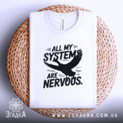 Футболка нервові системи білого кольору, складена на плетеній кошику, фон світло-сірий, принт чорного кольору з написом 'ALL MY SYSTEMS ARE NERVOUS.' та зображенням орла.